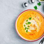 A creamy parsnip and carrot soup garnished with Greek yogurt and parsley, served with crusty bread.