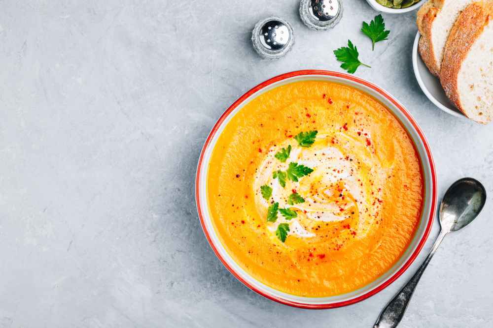 A creamy parsnip and carrot soup garnished with Greek yogurt and parsley, served with crusty bread.