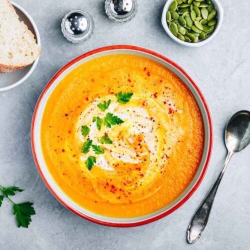 A creamy parsnip and carrot soup garnished with Greek yogurt and parsley, served with crusty bread.